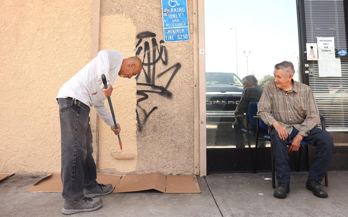 a man paints over graffiti as another man looks on