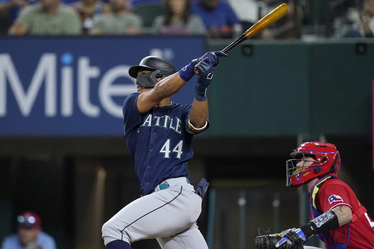 Seattle Mariners' Julio Rodriguez (44) follows through on a two-run single next to Texas Rangers catcher Jonah Heim during the fourth inning of a baseball game in Arlington, Texas, Friday, Aug. 12, 2022. (AP Photo/Tony Gutierrez)