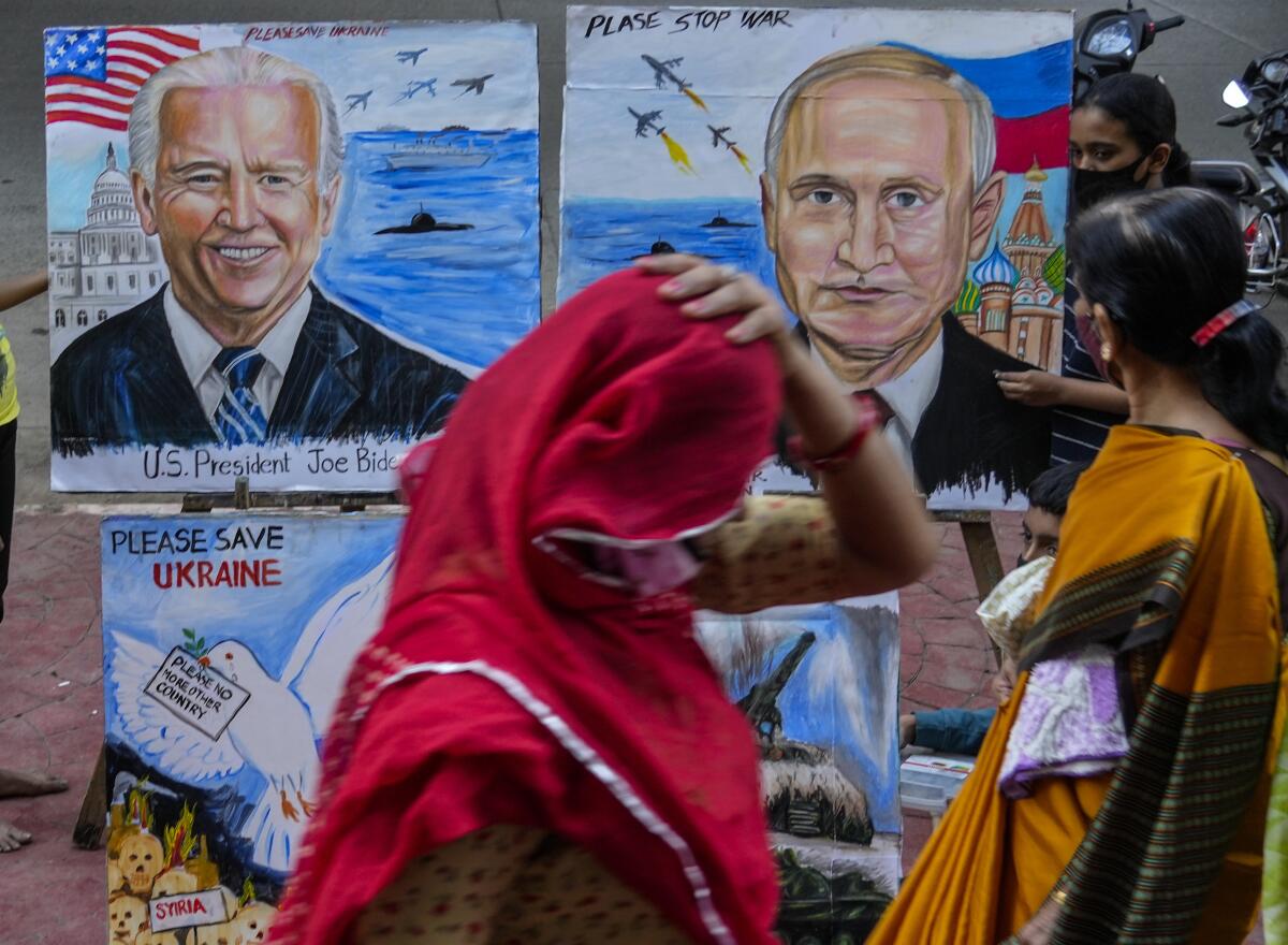 A woman walking past posters depicting President Biden and President Vladimir Putin