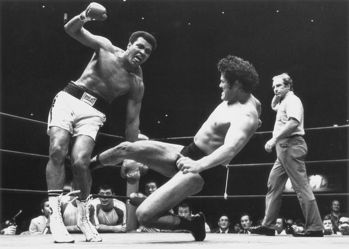 Wrestler Antonio Inoki, center, kicks boxer Muhammad Ali's leg in the ring as a referee and crowd look on