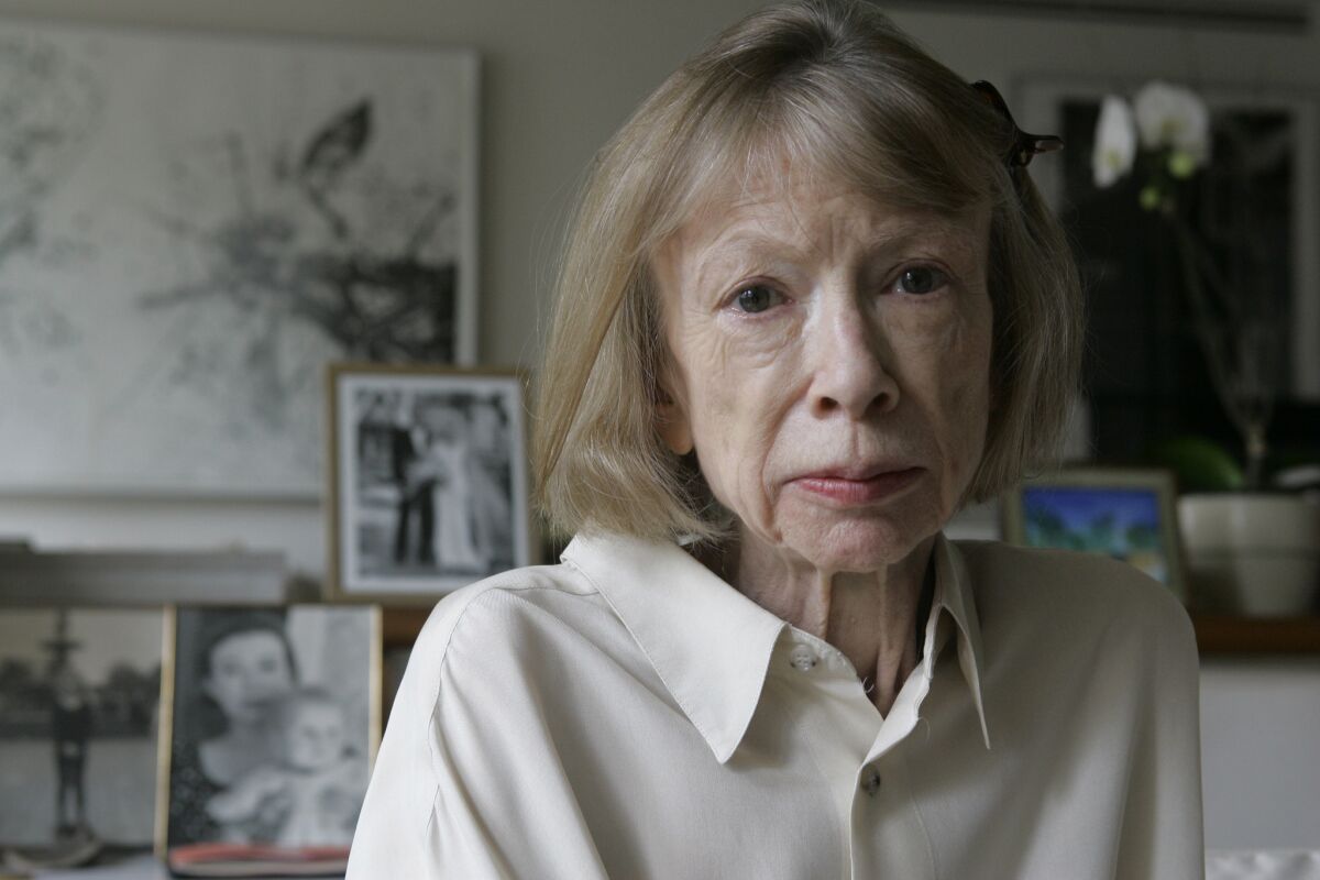 Joan Didion sits in front of a photo of herself holding her daughter, Quintana Roo, and another picture of her daughter's wedding, in her New York apartment on Sept. 26, 2005.