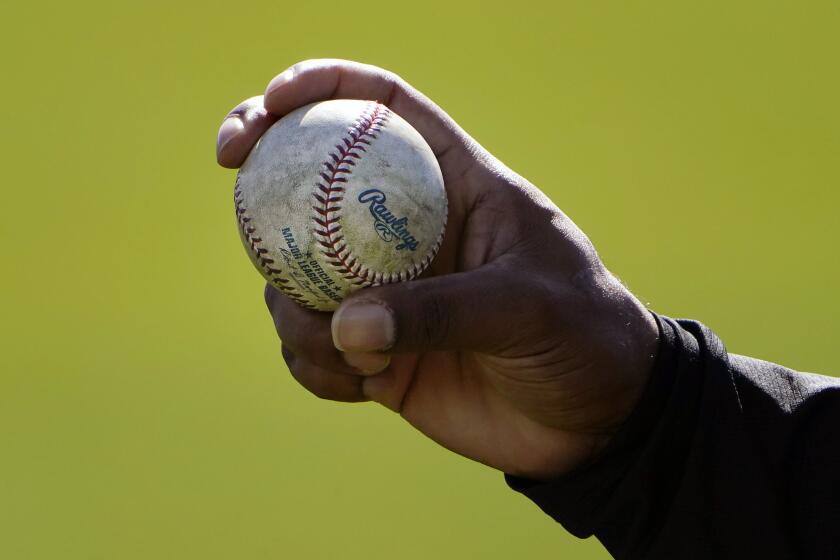 FILE - A Colorado Rockies pitcher shows his grip to a teammate during a spring training baseball workout in Scottsdale, Ariz., in this Wednesday, Feb. 24, 2021, file photo. Pitchers will be ejected and suspended for 10 games for using illegal foreign substances to doctor baseballs in a crackdown by Major League Baseball that will start June 21. The commissioner’s office, responding to record strikeouts and a league batting average at a more than half-century low, said Tuesday, June 15, 2021, that major and minor league umpires will start regular checks of all pitchers, even if opposing managers don’t request inspections. (AP Photo/Jae C. Hong, File)