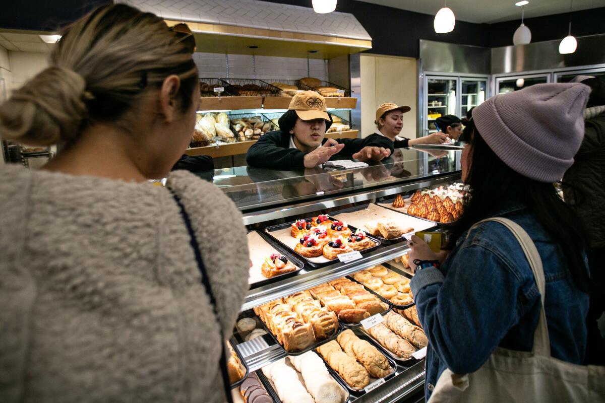 Women order from a pastry case in a bakery.