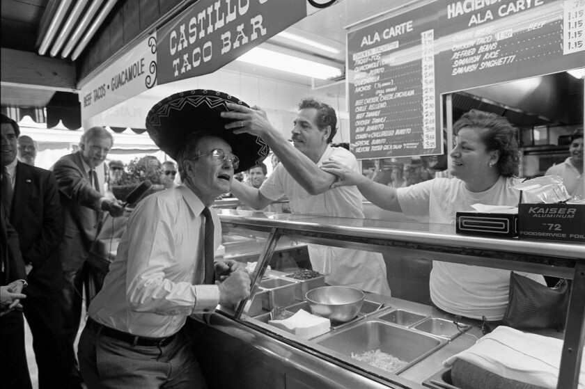 Workers at a taco shop place a sombrero on George Bush's head.