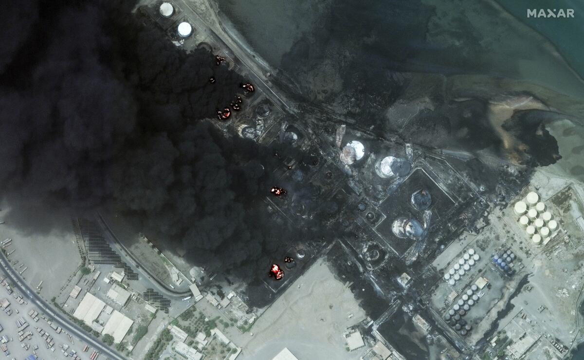 A satellite image shows smoke billowing from burning oil tanks.