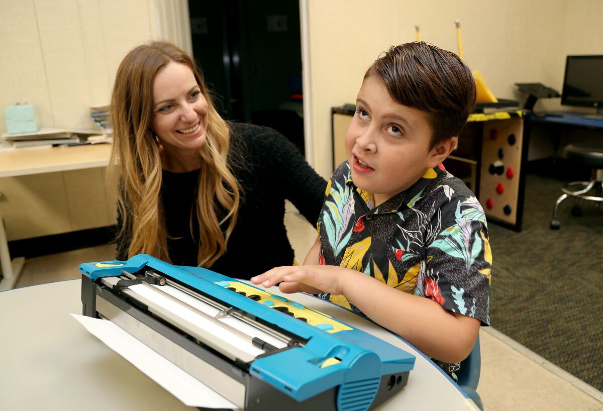 Mason Lopes, 11, of Santa Ana uses a Mountbatten Braille as his mother Charissa looks on at Beyond Blindness.