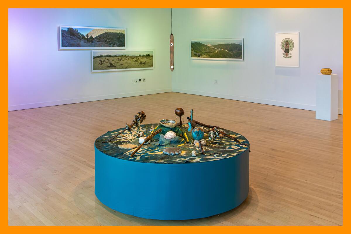 A museum gallery with wooden floors, an exhibit in the foreground and art on the walls in the background