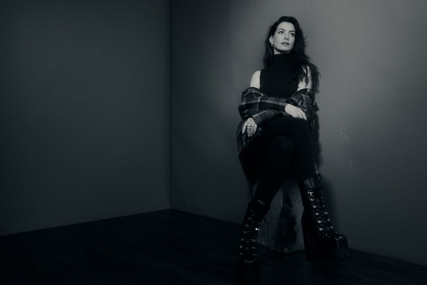  Anne Hathaway sits on a stool and poses against a wall, looking to her left