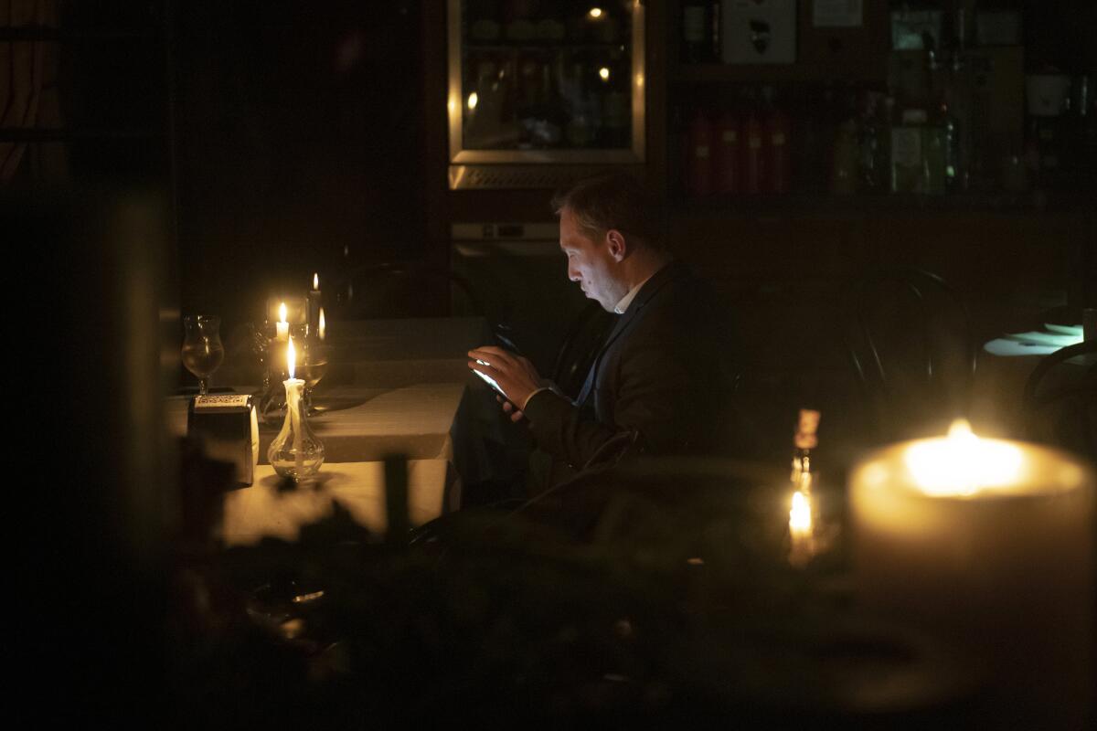 A man sits in a cafe during a blackout with lighted candles on tables.