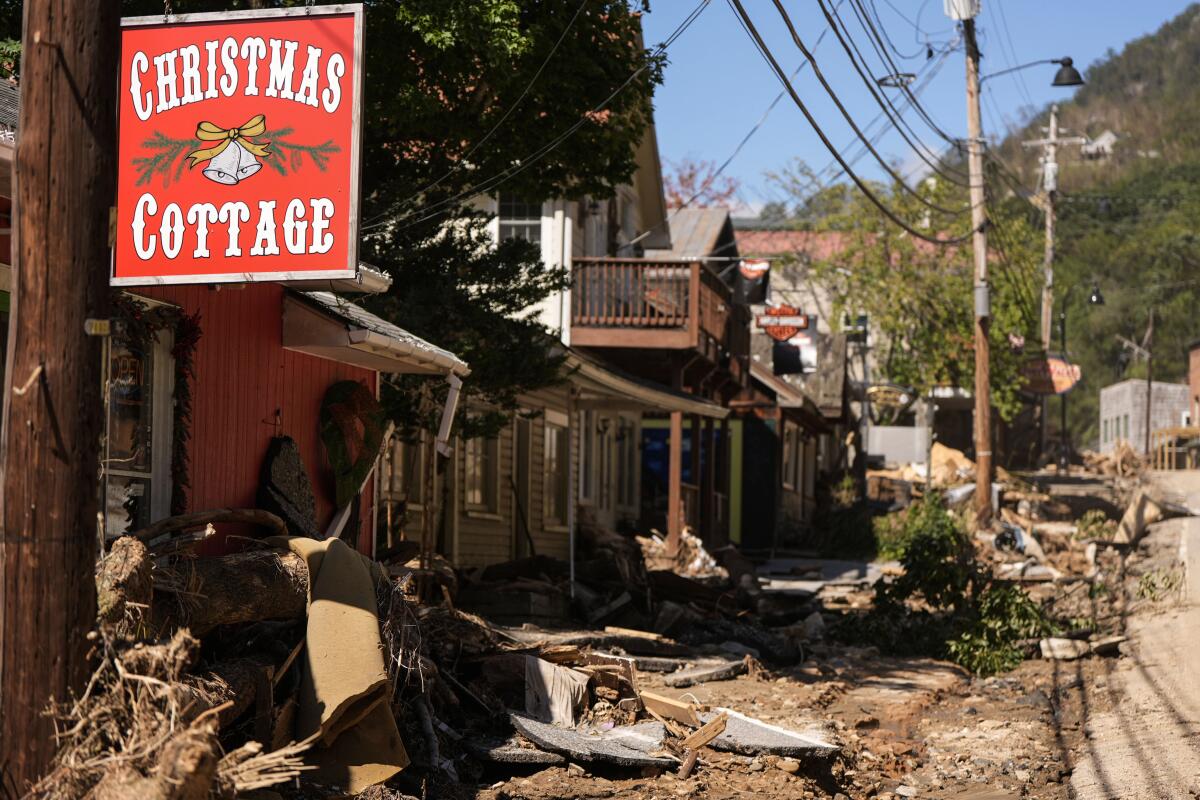 A red and white sign reading "Christmas Cottage" hangs from a pole, with flood debris in the background.