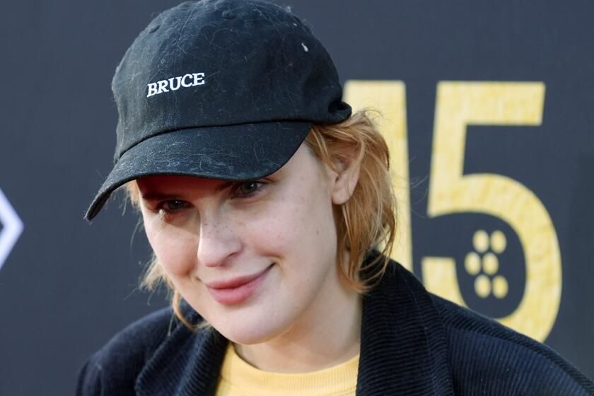 Tallulah Willis smirking wearing a dark hat with the word 'Bruce' on it. 