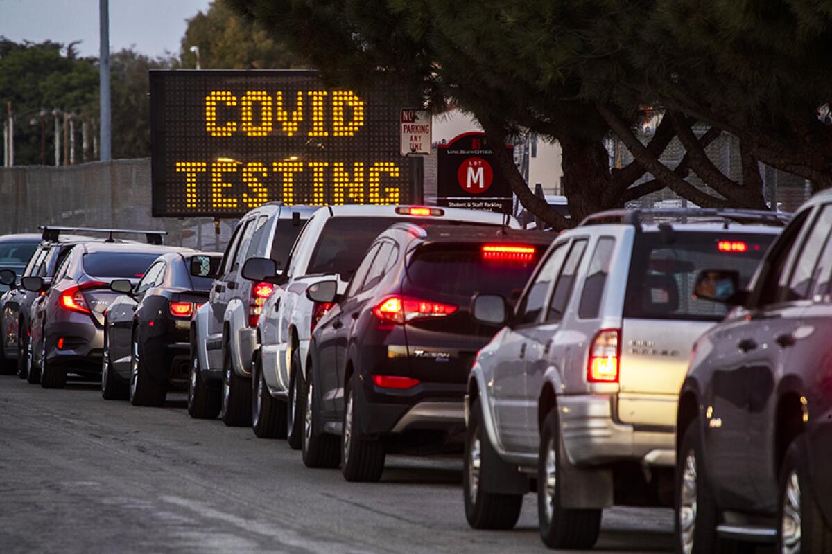 Cars line up in front of a sign that reads 'COVID TESTING.'