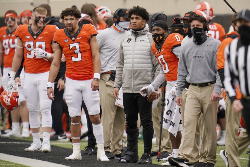 Oklahoma State running back Chuba Hubbard, center, watches from the sidelines wearing a boot on his right foot during an NCAA college football game against Texas Tech in Stillwater, Okla., Saturday, Nov. 28, 2020. From the left are Braden Cassity (90), Spencer Sanders (3), Hubbard, LD Brown (0), and head coach Mike Gundy. (AP Photo/Sue Ogrocki)