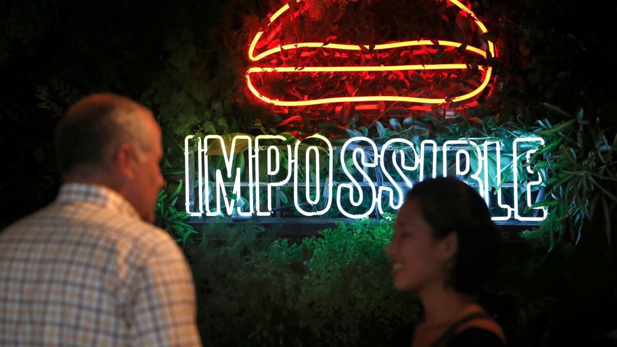 People talk in front of an impossible burger sign at an Umami Burger in downtown Los Angeles,