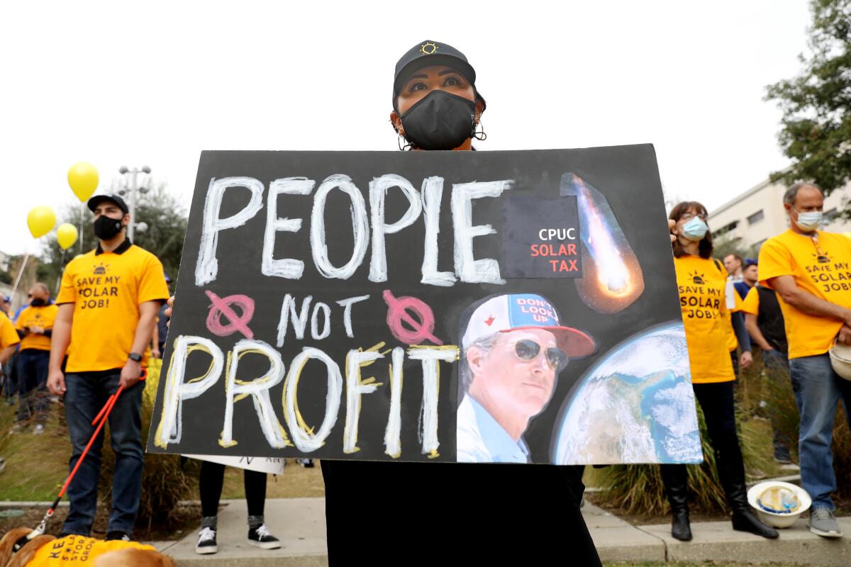 A woman holds a sign that says "People, not Profit" and has an image of Gavin Newsom.
