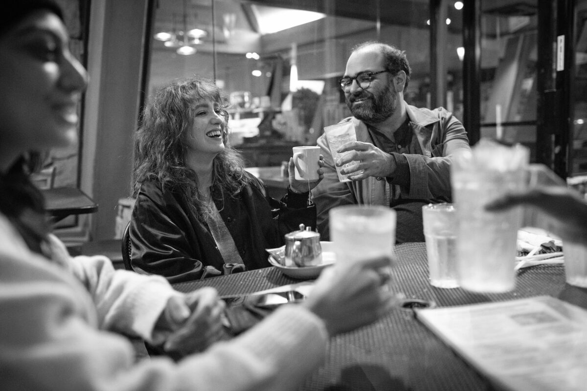 A black-and-white image of people sitting at an outdoor table, cheersing.