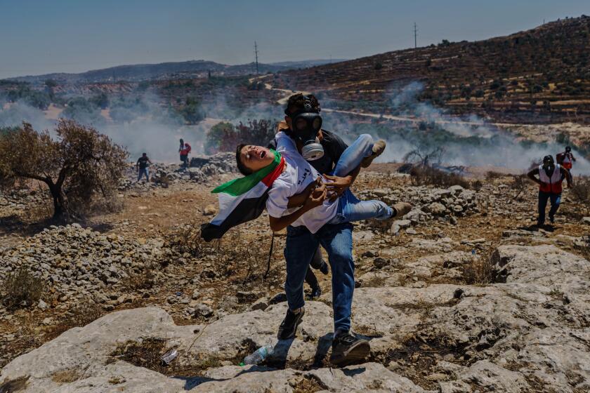 BEITA, PALESTINIAN TERRITORIES -- JUNE 25, 2021: A Palestinians struggling to breathe is carried away during a protest against West Bank Jewish settlement outpost Eviatar, that was recently established on the hilltop of Jabal Sabeeh adjacent to the village of Beita, near the city of Nablus, in occupied West Bank, Friday, June 25, 2021. Demonstrators have thrown stones, Molotov cocktails at Israeli security forces and soldiers have responded with tear gas, stun grenades and live ammunition. (MARCUS YAM / LOS ANGELES TIMES)