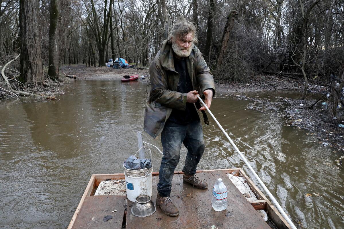 An unhoused man uses a raft to move his belongings from his tent at a homeless encampment on Bannon Island.