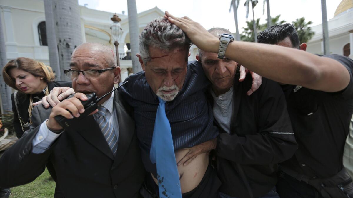 Opposition lawmaker Americo de Grazia is led away by bodyguards and a National Assembly employee after he was injured in a melee with protesters who tried to force their way into the legislature.
