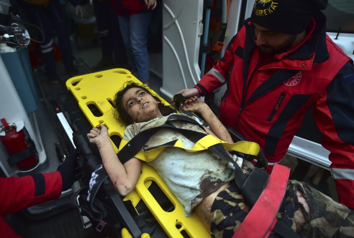 A young girl is carried on a stretcher to an ambulance after being pulled from rubble.