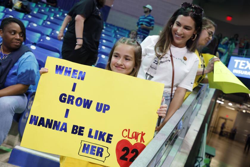 CORRECTS FROM CAITLYN TO CAITLIN - Pailynn Amos, center, holds a sign for Indiana Fever guard Caitlin Clark in front of her mother Rebecca Amos, of Ennis, Texas, prior to an WNBA basketball game against the Dallas Wings in Arlington, Texas, Friday, May 3, 2024. (AP Photo/Michael Ainsworth)