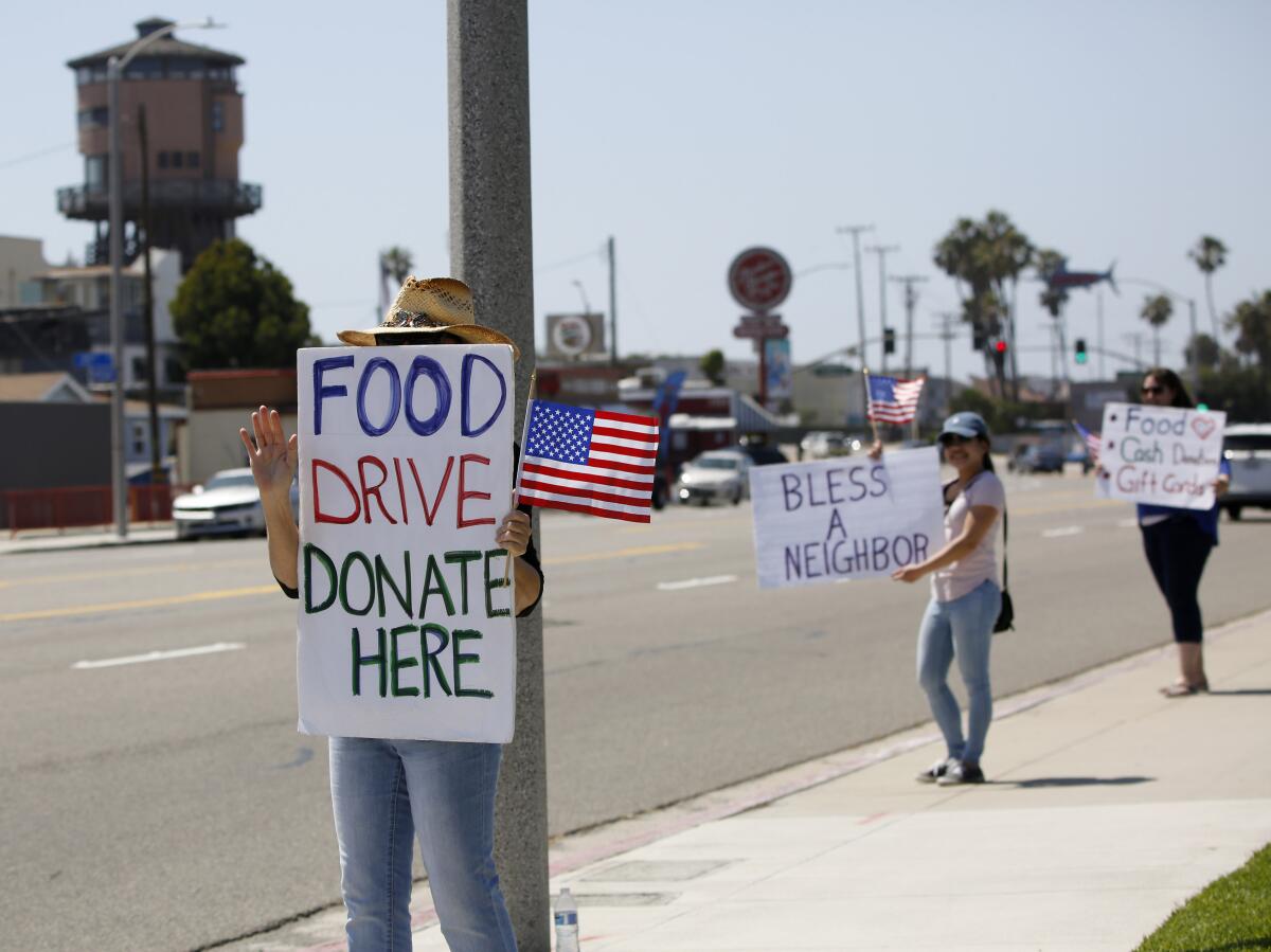 People stand on a sidewalk with signs promoting a food drive.