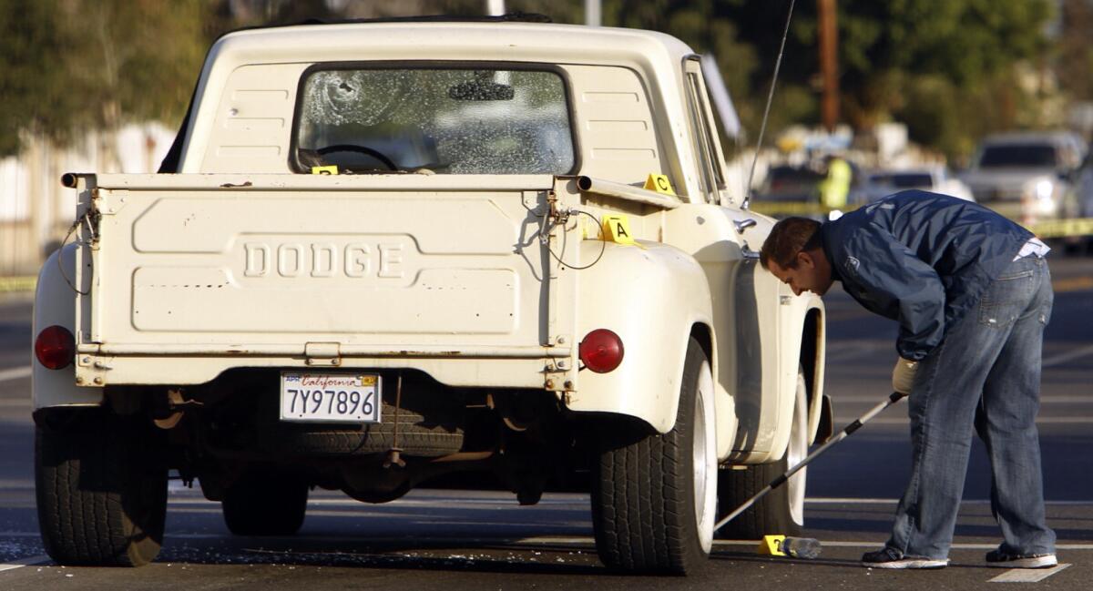 An LAPD investigator inspects a Dodge truck with several bullet holes sitting in the intersection of Glenoaks Boulevard and Vaughn Street in Pacoima.