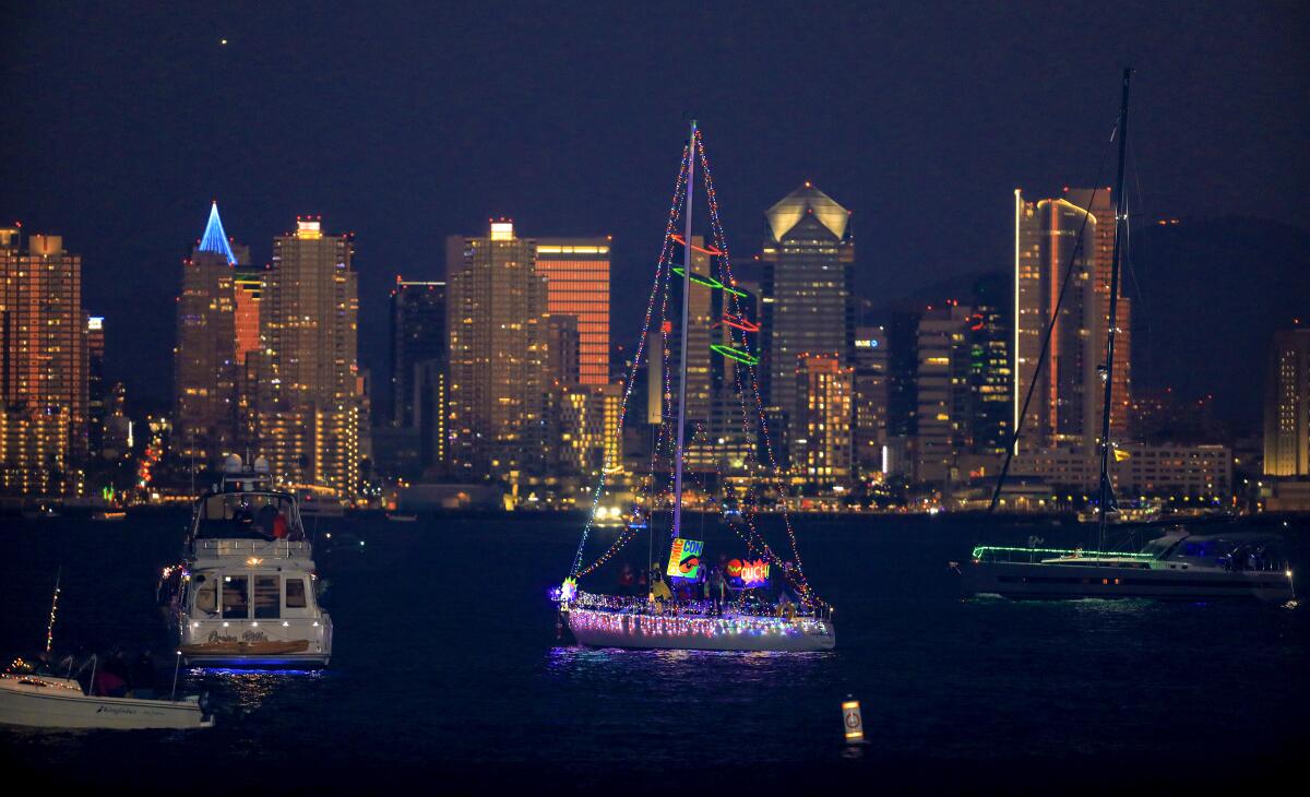 Boats covered in lights sail past the illuminated San Diego skyline