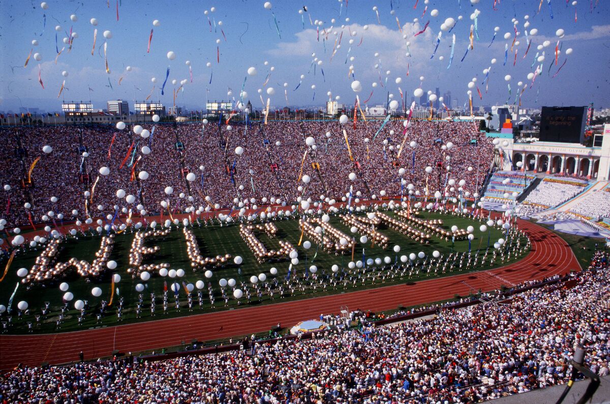 An aerial view of a packed stadium, balloons filling the air and people spelling out the word "welcome" on the field.