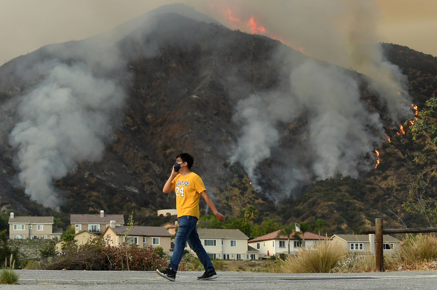 A man walks by a row of homes as the Ranch fire is seen in the background