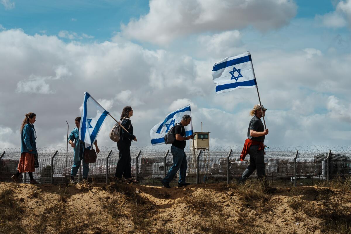 A small group, including three people holding Israeli flags, walking near a high-security fence