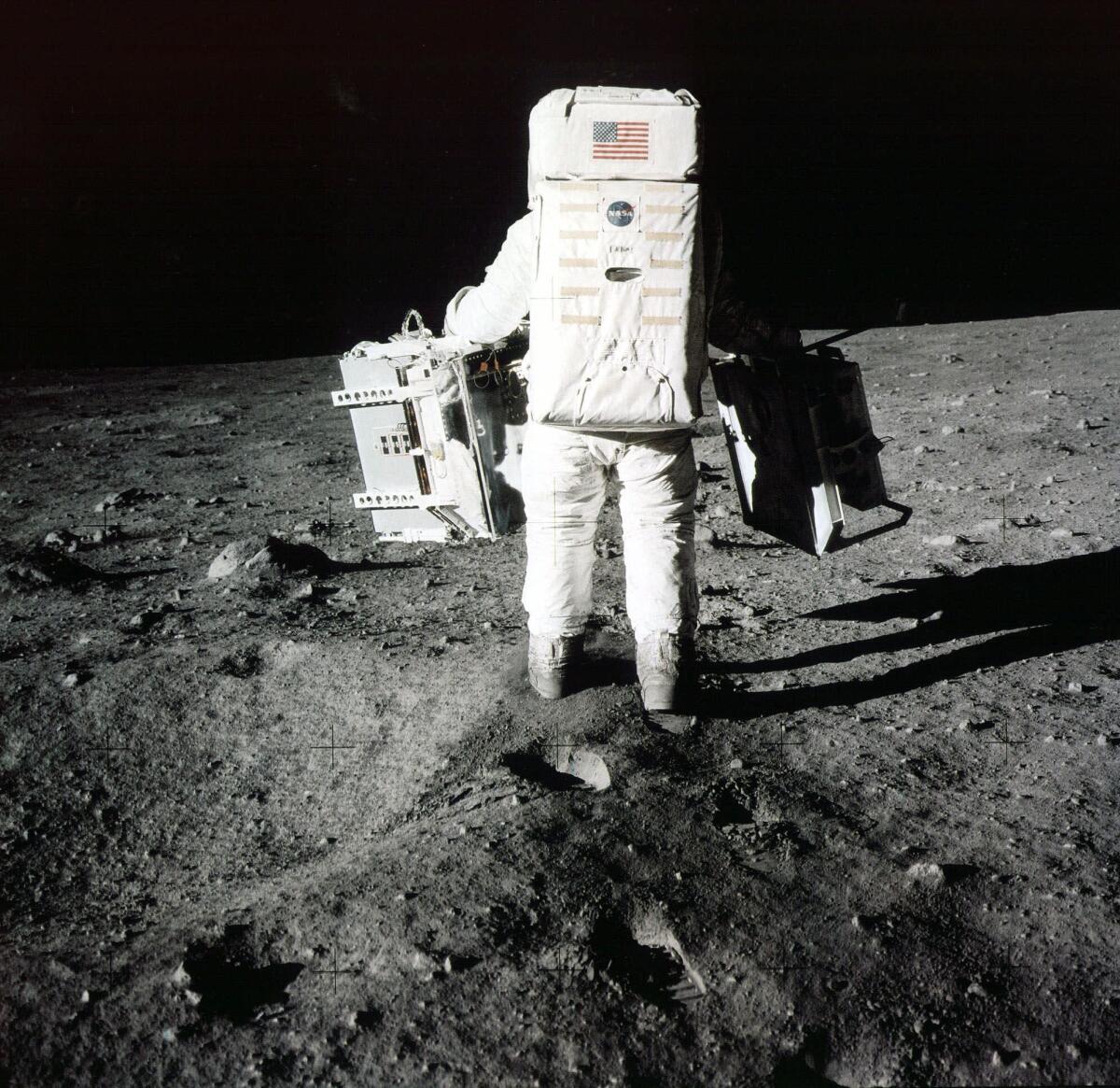 Buzz Aldrin carries scientific experiments on the moon. The picture was taken by Neil Armstrong.