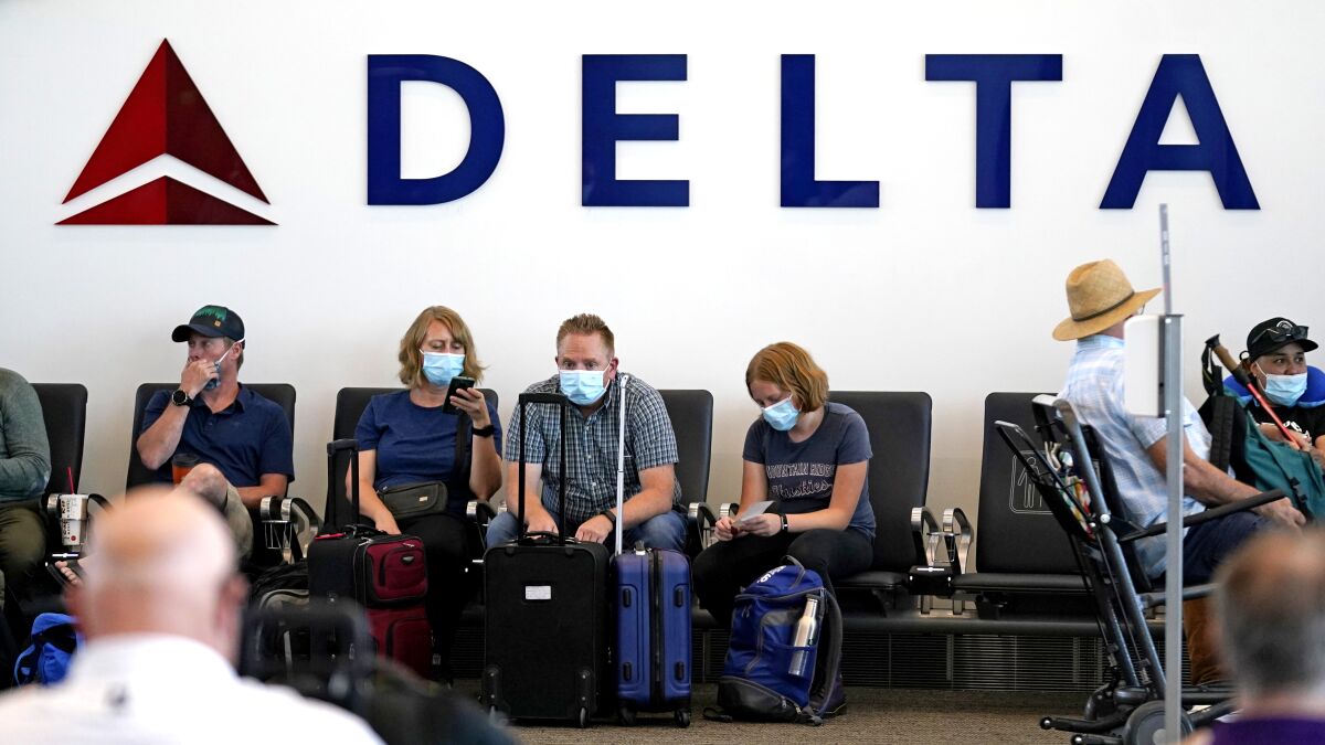 Passengers sit under a Delta sign at an airport.