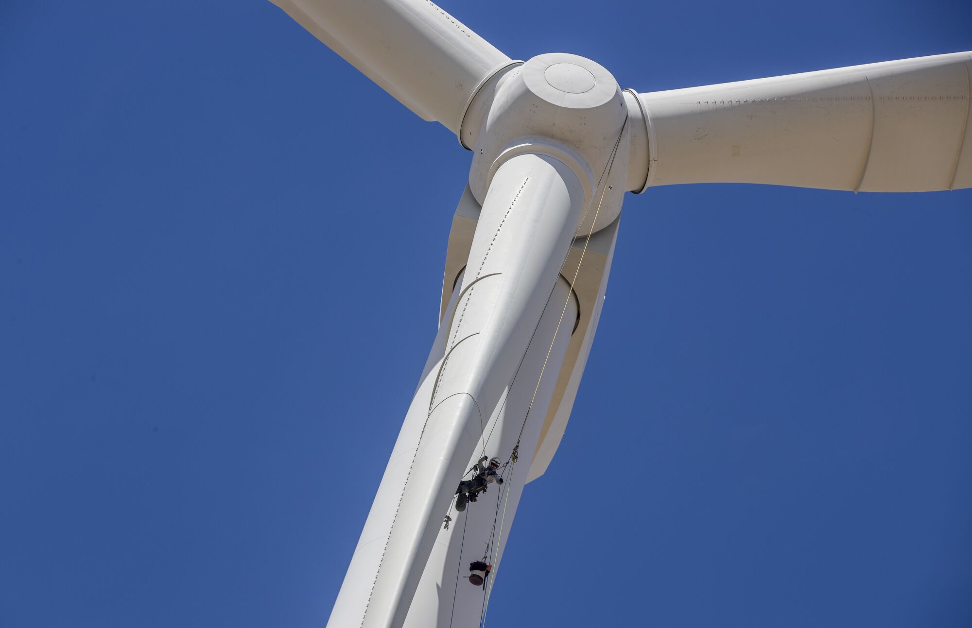 A man hangs from a wind turbine.