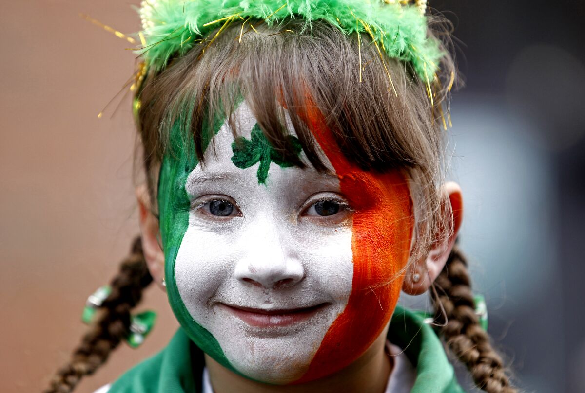 A girl in pigtails with her face painted in the colors of Ireland's flag. 