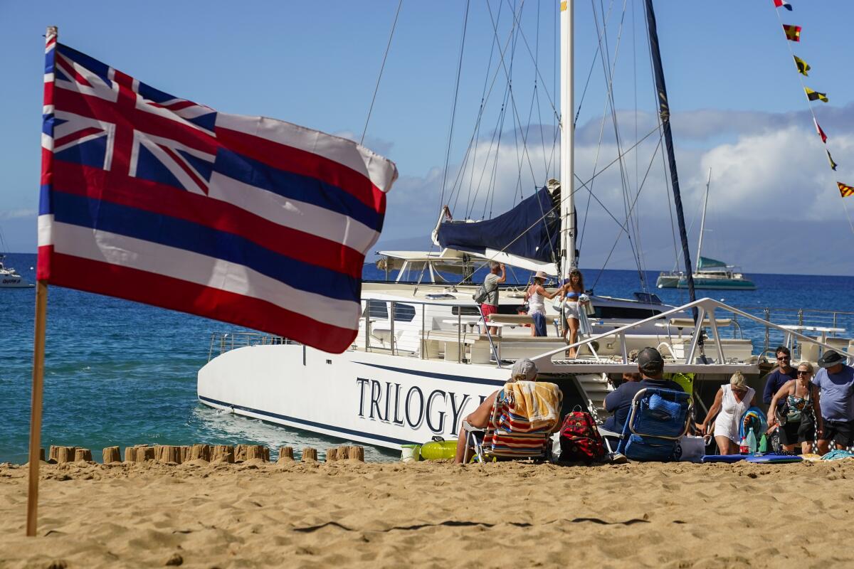 Tourists get off of a Trilogy Excursions boat arriving on Kaanapali Beach in front of a flag of Hawaii planted in the sand.