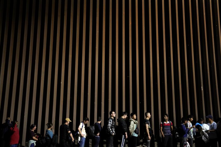 FILE - People line up against a border wall as they wait to apply for asylum after crossing the border from Mexico, July 11, 2023, near Yuma, Ariz. An appeals court Thursday, Aug. 3, allowed a rule restricting asylum at the southern border to stay in place. The decision is a major win for the Biden administration, which had argued that the rule was integral to its efforts to maintain order along the U.S.-Mexico border. (AP Photo/Gregory Bull, File)