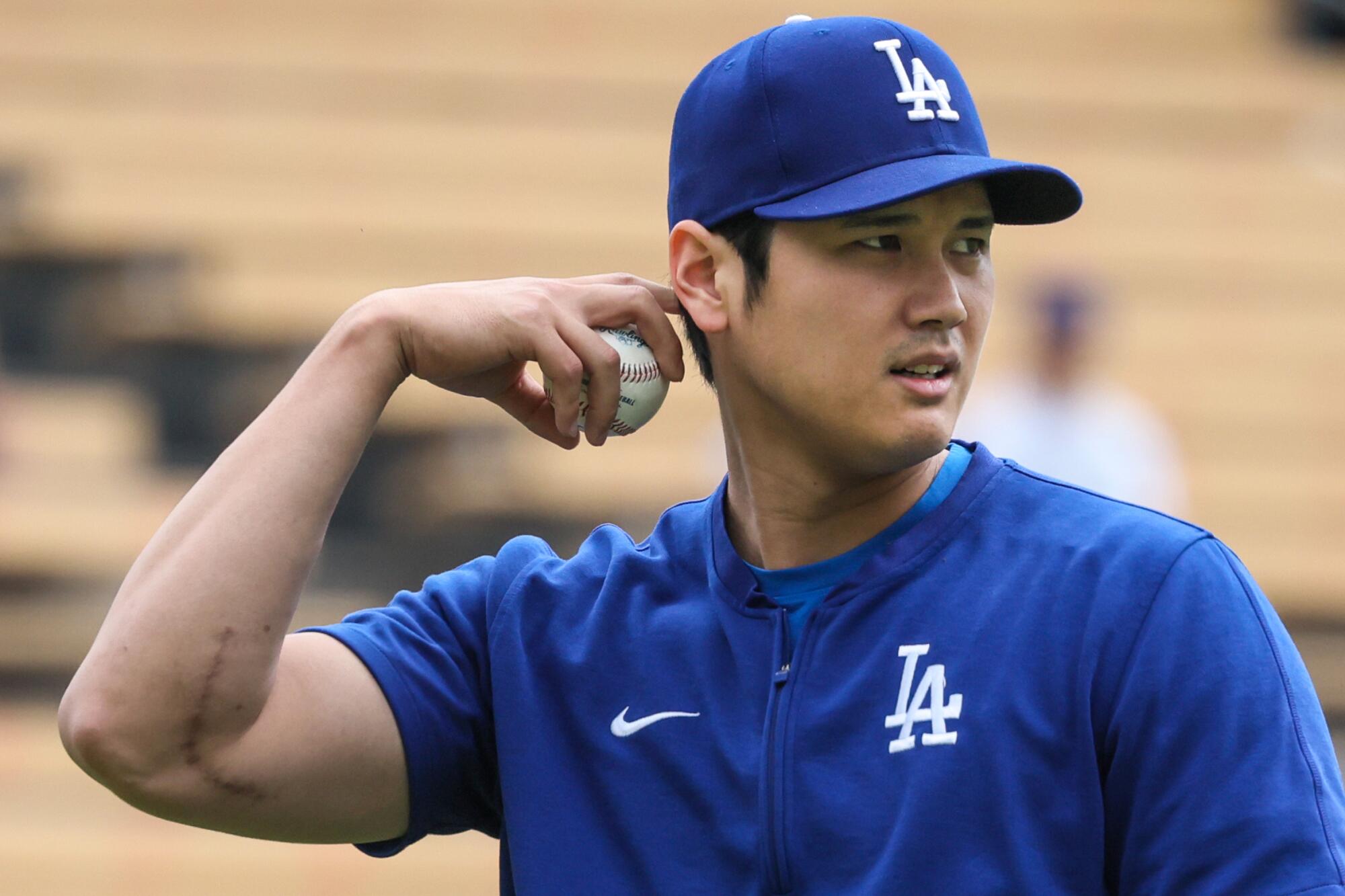 Dodgers two-way player Shohei Ohtani holds a baseball, his right arm flexed.