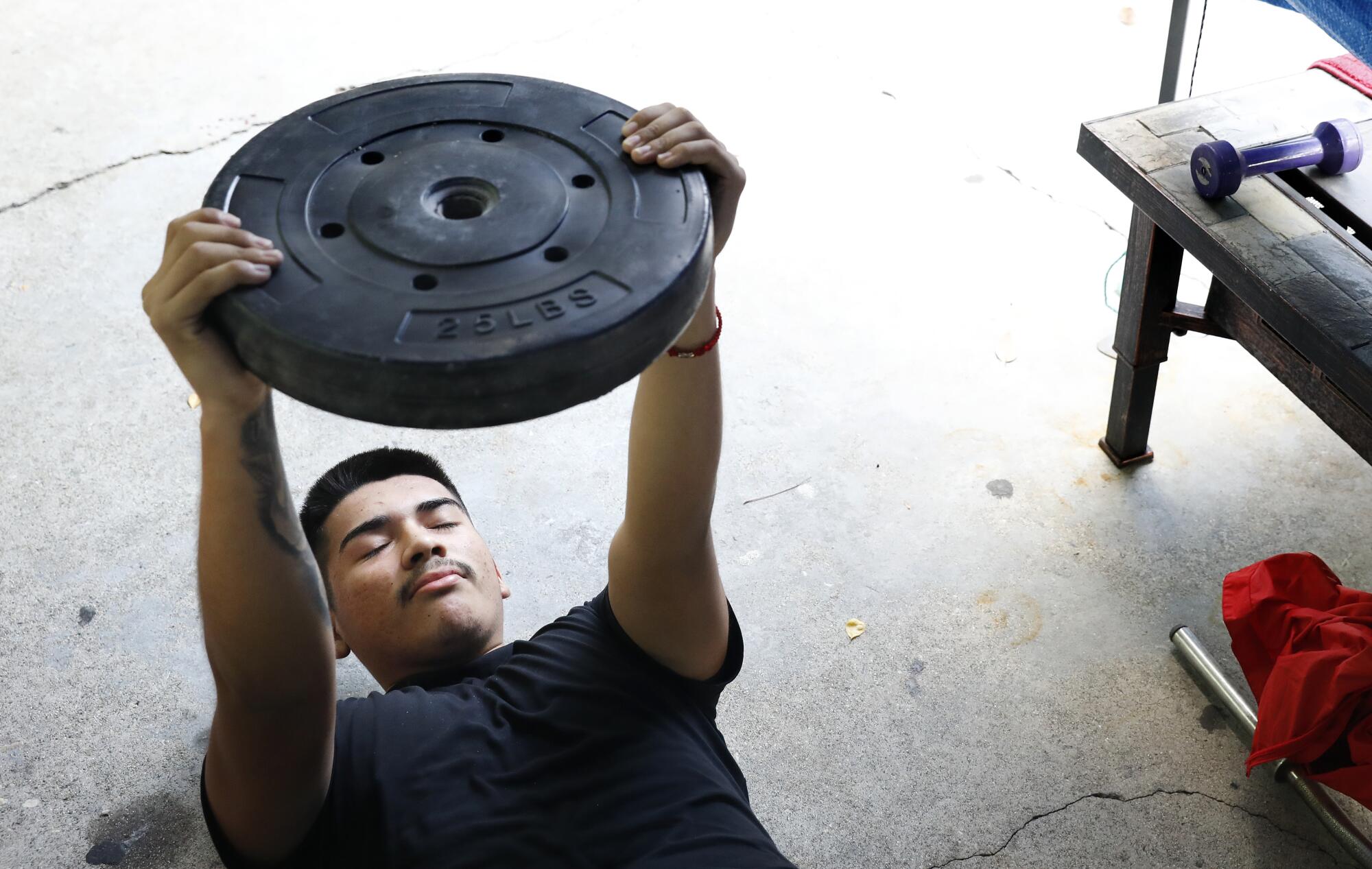 East L.A. Roosevelt's Damian Avalos lifts a weight during a remote team workout at his home.