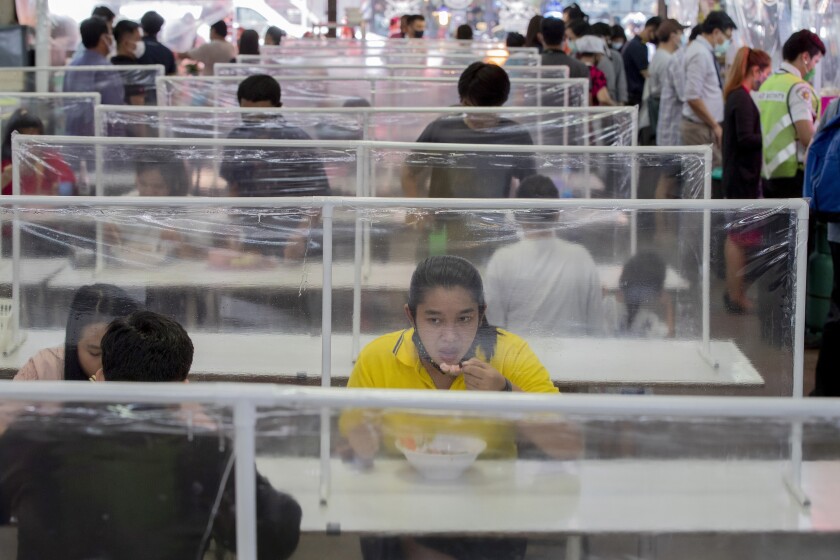 Clientes comen en un patio de comidas en mesas comunes separadas por pantallas de plástico en Bangkok