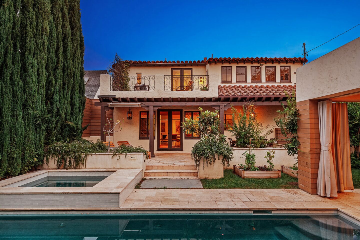 The Spanish Colonial-style home boasts charming outdoor spaces including a landscaped courtyard and a backyard with a pool and movie screen surrounded by fruit trees.