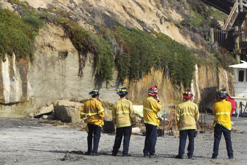 Firefighters look at a section of oceanfront bluff that collapsed killing one woman and injuring three just north of the Grandview beach access stairway in Leucadia on Friday, August 2, 2019 in Encinitas, California.