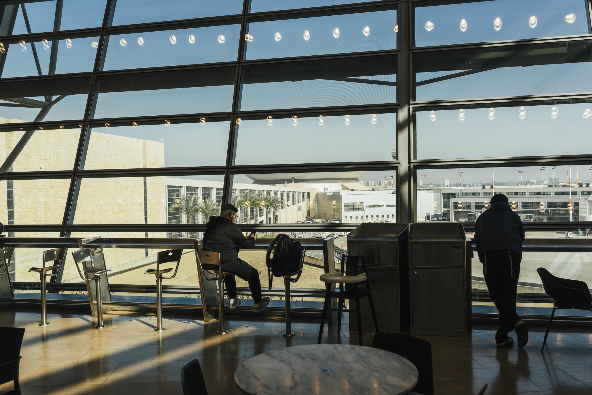 A man sits in an airport lounge with glass windows facing buildings