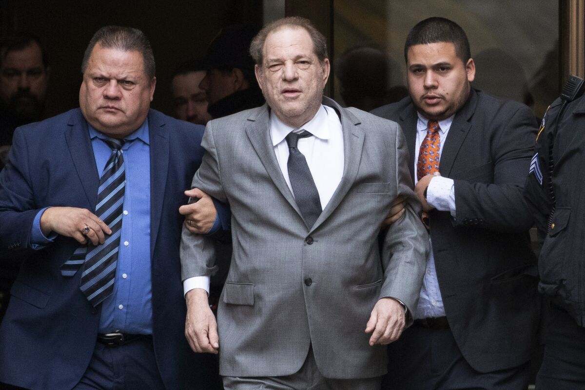 Men hold Harvey Weinstein's arms as he leaves court.