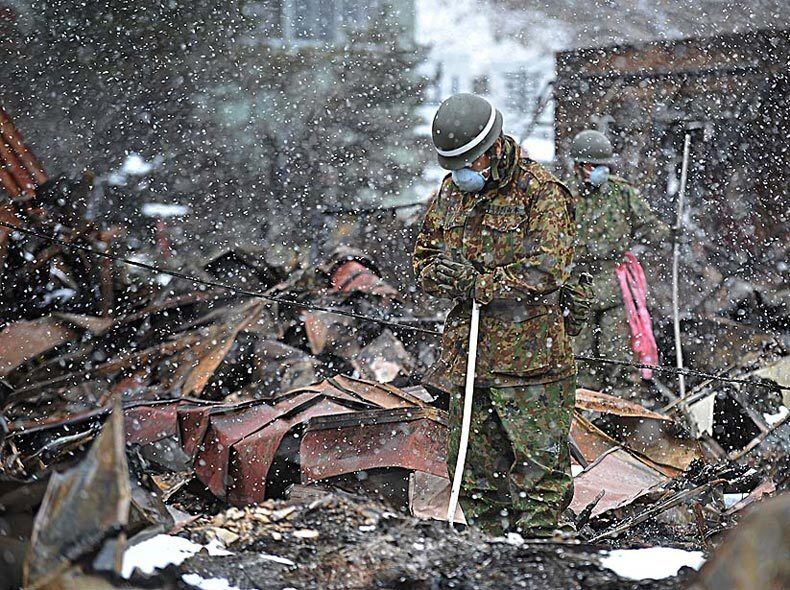 A Japanese Self-Defense Force soldier prays before removing the body of a tsunami victim found in debris in Otsuchi.
