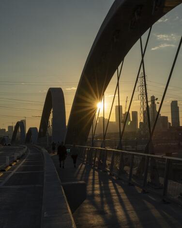 The 6th Street Bridge at sunset, its arches lighted red and white, with L.A.'s skyline in the background.