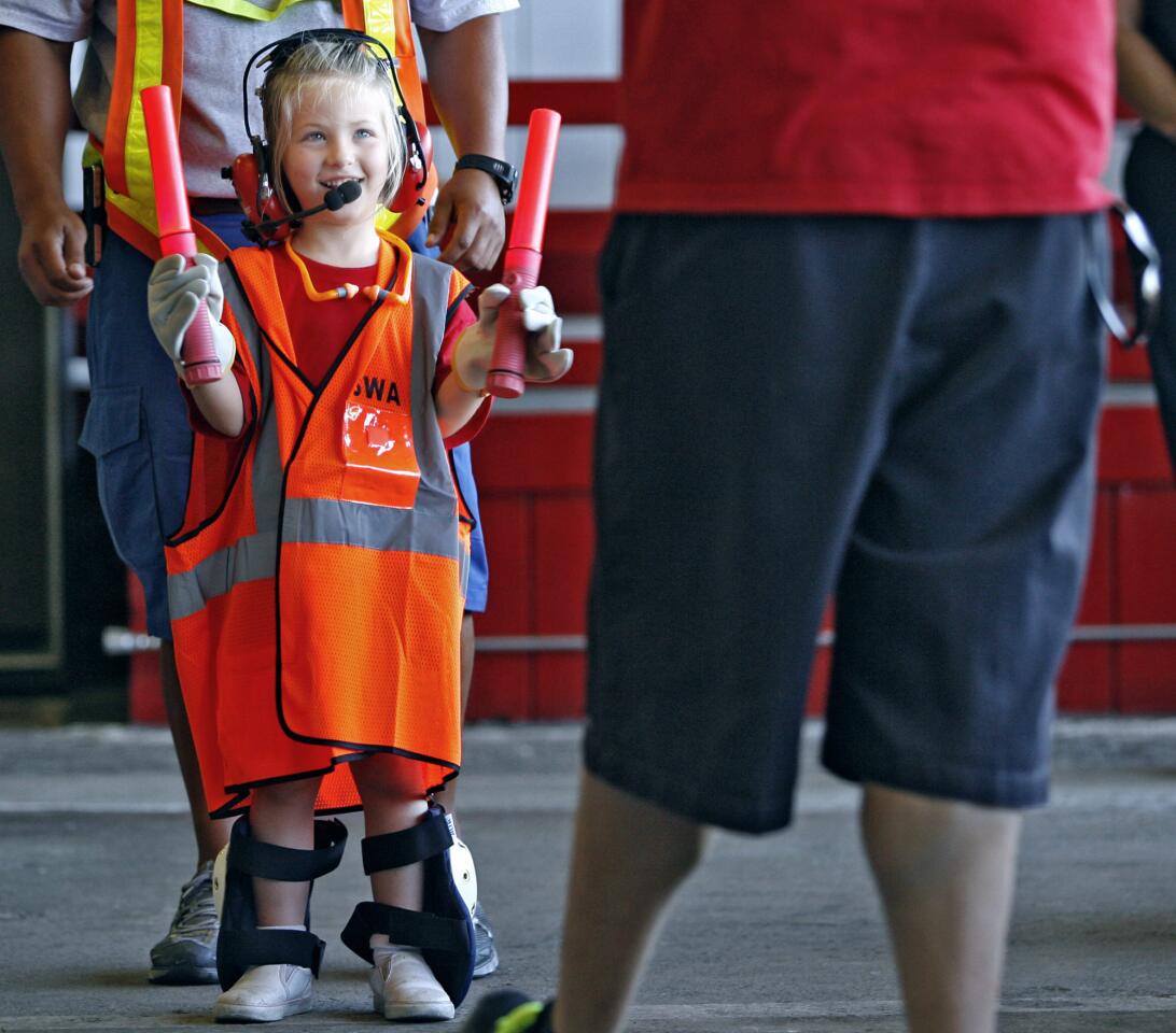 Wearing Southwest Airlines ground crew equipment, 6-year-old Emmy De Oliveira learns how to guide an airplane using a person during the Robert Gross Park Camp visit to the Bob Hope Airport in Burbank on Thursday, July 19, 2012. Sixty-five children visited the airport's fire station and learned about airport careers.