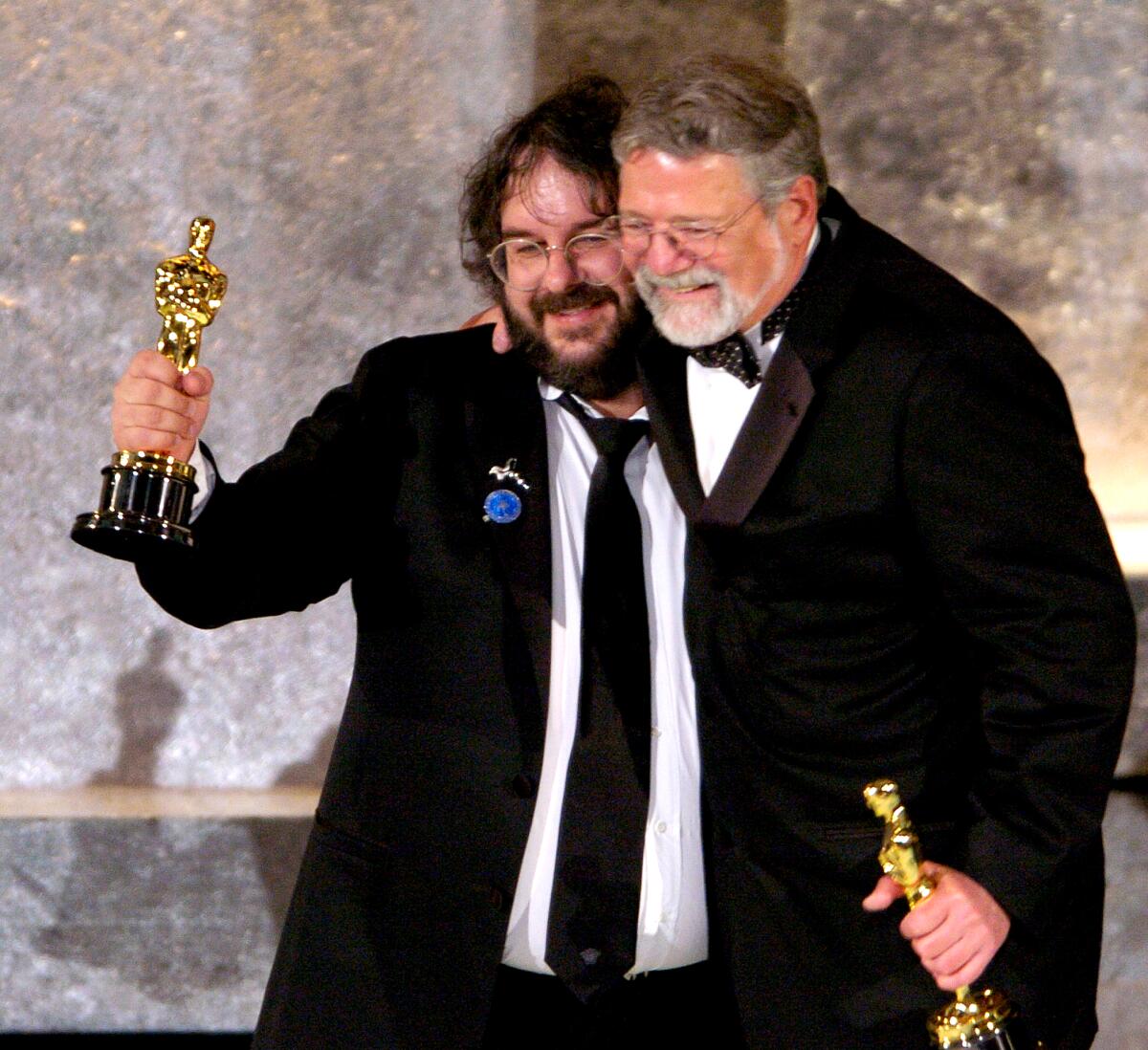 Two bearded men in tuxedos embrace as they hold their Oscars.