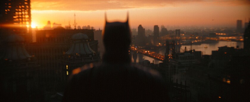 Ein Schuss von hinten von Batman auf einem Dach mit Blick auf die Skyline der Stadt.