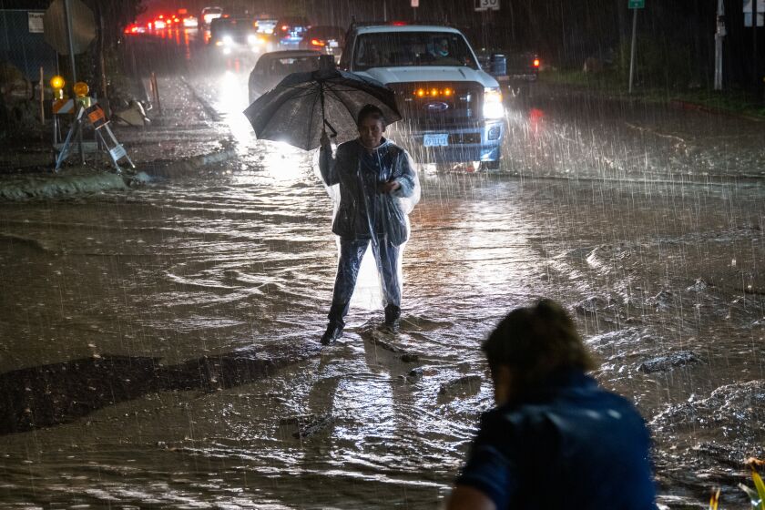 MONTECITO, CA - JAN. 9, 2022: Rosa Gallardo crosses a flooded street in Montecito after getting off work at her hotel job. (Michael Owen Baker / For The Times)